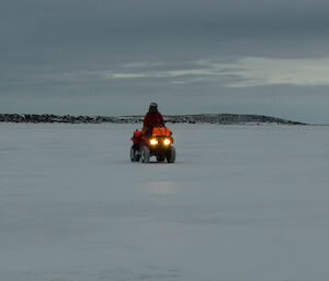 Expeditioner riding a quad bike on the sea ice with the sun setting behind her