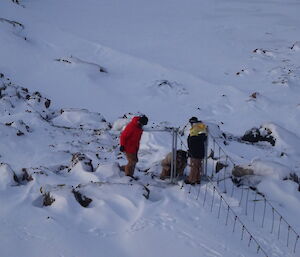 Three expeditioners with tools releasing tension on snow covered swing bridge