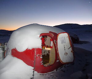 Looking from outside in, expeditioner inside a small hut with a fire extinguisher