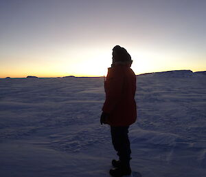 Expeditioner in the sea ice facing a stunning sunrise