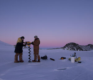Two expeditioners on the sea ice holding a jiffy drill