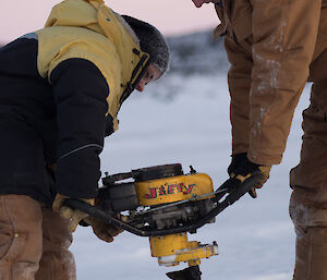 Two expeditioners drilling through thick ice on a lake