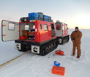 Expeditioner standing alongside a Hägglunds ready to drill a hole in the sea ice