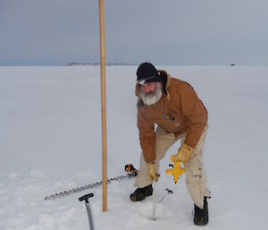 Expeditioner lowering a measuring tape through a hole in the sea ice