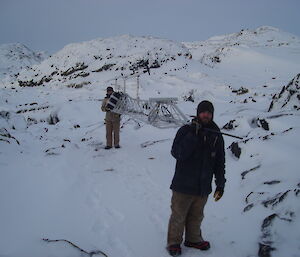 Two expeditioners carrying a large antenna across rocks and snow