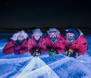 Four expeditioners laying on a frozen lake lit up from beneath the ice