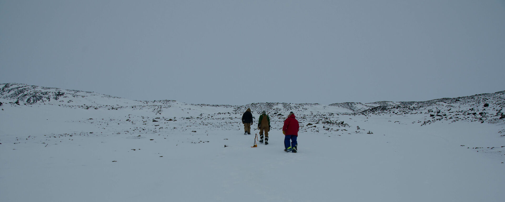 Three expeditioners walking on snow-covered ground towards a hill