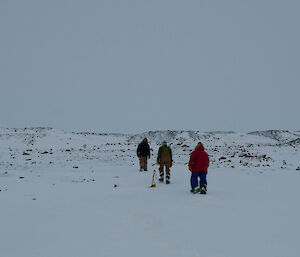 Three expeditioners walking on snow-covered ground towards a hill