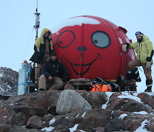 Three expeditioners standing next to a round, red fibreglass hut