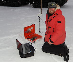Expeditioner kneeling on the sea ice with his laptop connected to a stress buoy