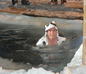 Expeditioner wearing a cow outfit swimming in a cut out hole in the sea ice