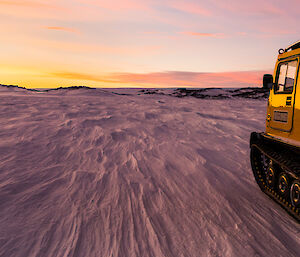 Yellow Hägglunds facing into a sunrise and an icy plateau