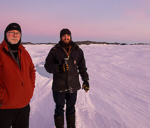 Two expeditioners standing on the sea ice in the dark one holding a coffee