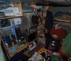 Expeditioner sitting in front of a heater in a crammed hut