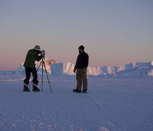 Expeditioner taking a photo of friend on the sea ice surrounded by iceburgs