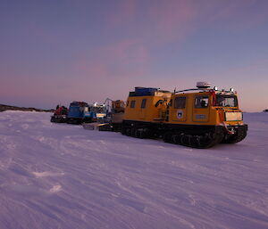 Two Hägglunds parked on the sea ice sunset in background