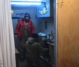 Two expeditioners in a hut working on a small oven