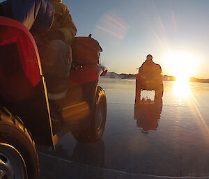 Two expeditioners on riding quad bikes on a smooth frozen lake