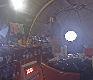 Expeditioner standing by the stove inside a hut