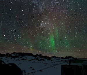 Thousands of stars and a green aurora above a small hut