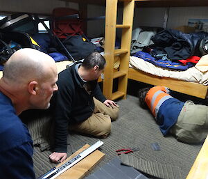 Three expeditioners laying carpet tiles in a small hut