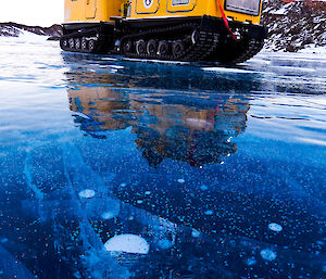 Yellow hagglunds parked on a smooth blue frozen lake