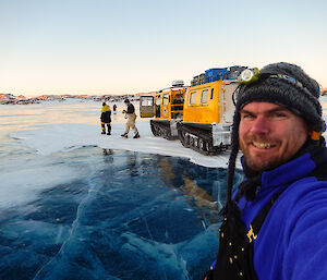 Expeditioner taking a photo of himself with 3 others in the background, a yellow hagg on a frozen blue lake
