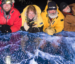 Four expeditioners on laying on a frozen lake at night, with lights under the ice
