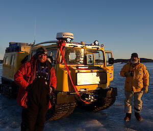 Two expeditioners standing on a frozen lake alongside a yellow hagg