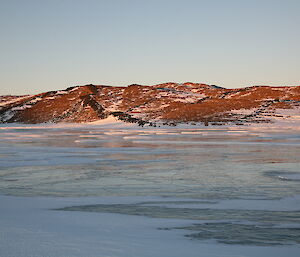 Smooth frozen lake with the sun shining on the hills in the background