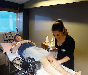 Expeditioner laying on table with a female preparing to wax his legs