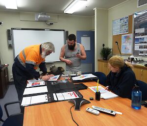 Three expeditioners gathered around a conference table with maps discussing a plan of action