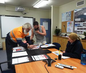 Three expeditioners gathered around a conference table with maps discussing a plan of action