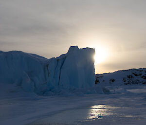 Large blue ice berg the sun trying to shine through thick grey cloud