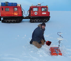 Expeditioner on the sea ice kneeling over a grey case full of electronic equipment