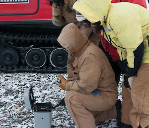 Four expeditioners standing over the small grey HF radio and grey case