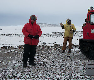 Two expeditioners standing alongside a hagglunds with HF radio cables