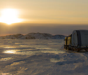 Yellow Hägglunds towing a mobile tent on a sled on the sea ice
