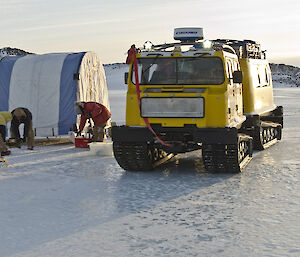Expeditioners drilling holes in the lake ice alongside the mobile tent