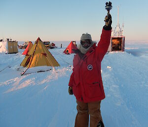 Expeditioner with her arm raised high with an instrument in her hand which reads the wind speed