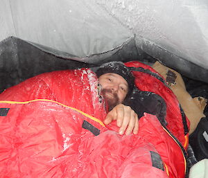 Expeditioner in sleeping bag covered in ice and snow,