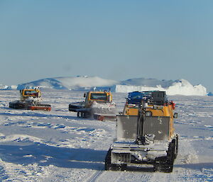 Vehicles following single file in the sea ice with a large ice berg in the background