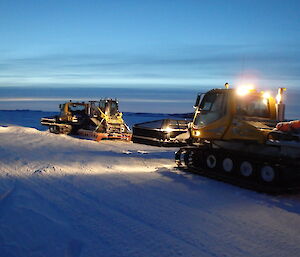 Two snow groomers following each other at night