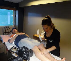 Male laying on a table with female preparing to wax his legs