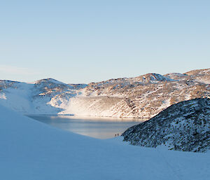 Snow covered valley and hills and a lake in the middle of the photo. Two guys in the distance near the lake