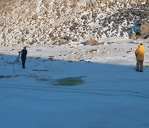 Two expeditioners in a snow covered valley pulling in ropes