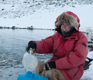 Expeditioner sitting alongside a lake pouring lake water into a container