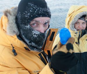 Close up photo of two people near a lake holding a blue container lid