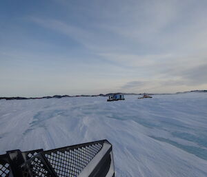 Two vehicles following in each other on the sea ice, ice bergs in the background