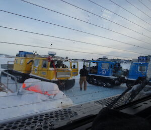 Photo taken form inside a vehicle looking towards two parked hagglunds on the sea ice